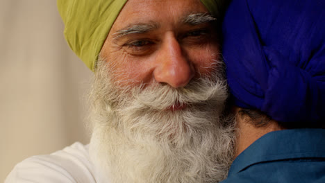 Close-Up-Studio-Shot-Of-Senior-Sikh-Father-Embracing-Adult-Son-Both-Wearing-Turbans-Against-Plain-Background-2